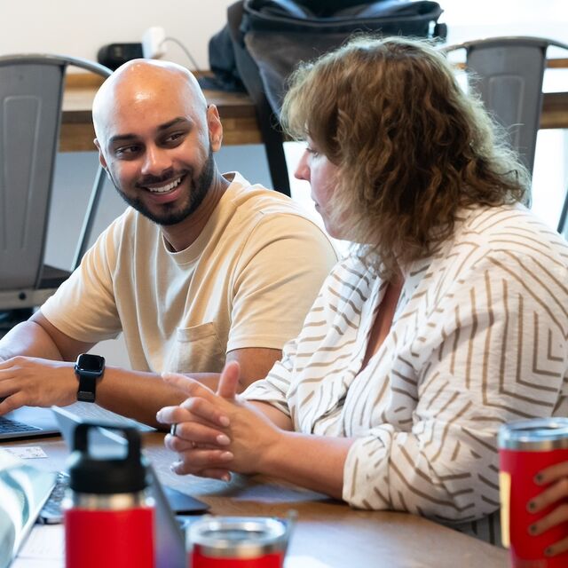 Person typing on laptop while smiling to the person next to them