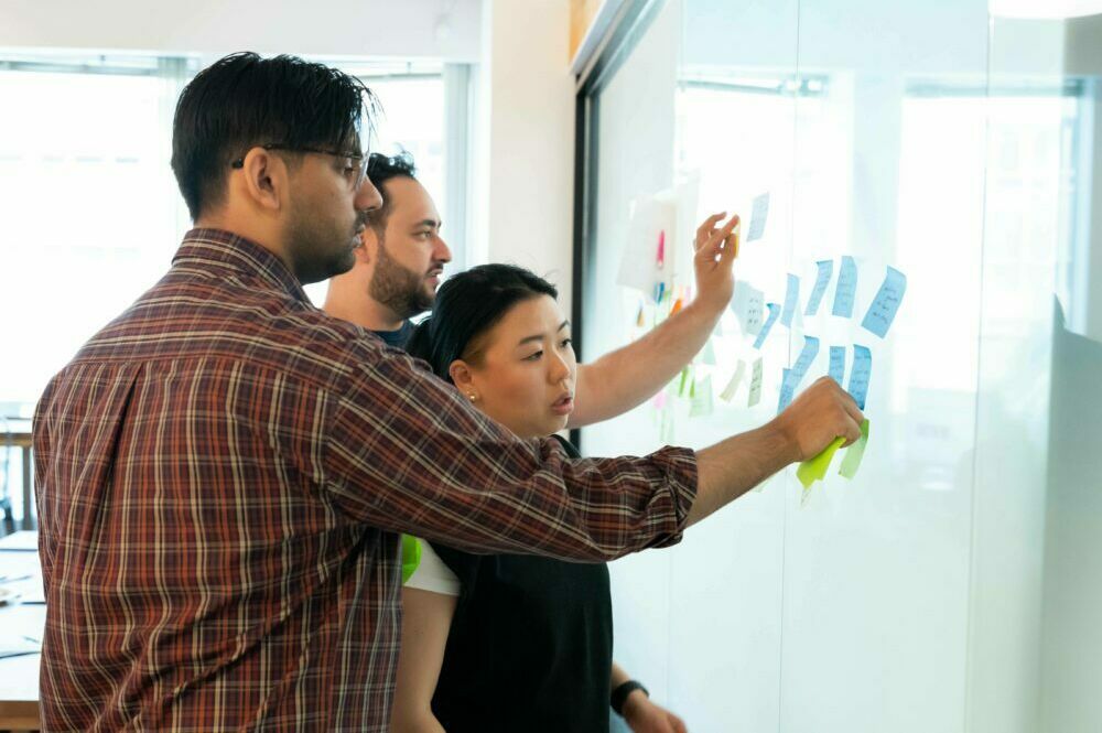 Three team members scheming with sticky notes at a whiteboard